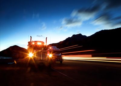 Illuminated headlights of semi-truck against sky at dusk