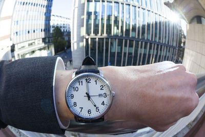 Cropped hand of businessman wearing wristwatch by railing in city