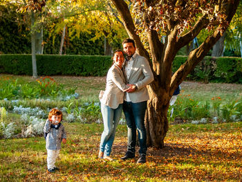 Portrait of smiling couple with son standing against tree in park