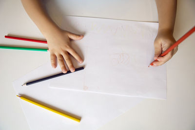 Boy child in a blue t shirt on yellow background sits at  white table and draws with colored pencils