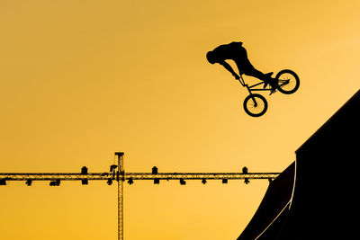 Low angle view silhouette of man performing stunts on bicycle against sky during sunset