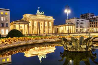 The famous brandenburger tor in berlin at night, reflected in a fountain