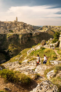 People sitting on rock by mountain against sky