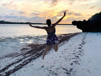 Full length of young woman at beach against sky during sunset