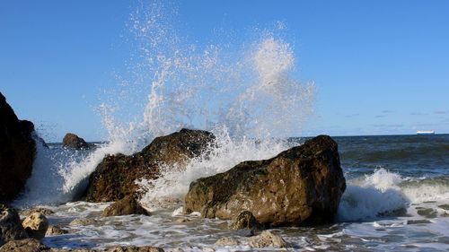 Waves splashing on rocks at sea shore against sky