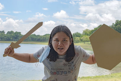 Portrait of woman standing against sky with cardboard sword and shield