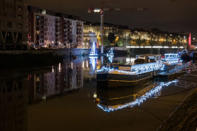 Boats moored in illuminated city against sky at night