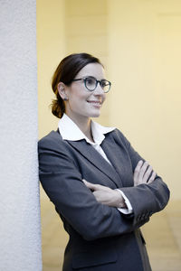 Smiling businesswoman with arms crossed leaning on wall