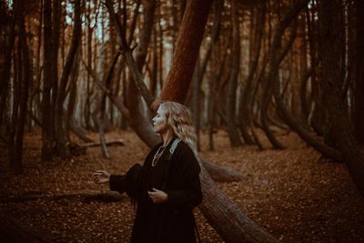 Woman standing by tree trunk in forest