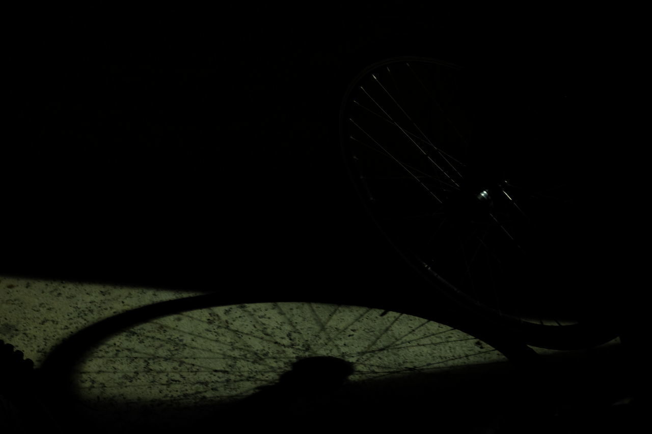 CLOSE-UP OF BICYCLE WHEEL AGAINST DARK BACKGROUND
