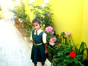 Portrait of girl in school uniform standing by flowers at yard