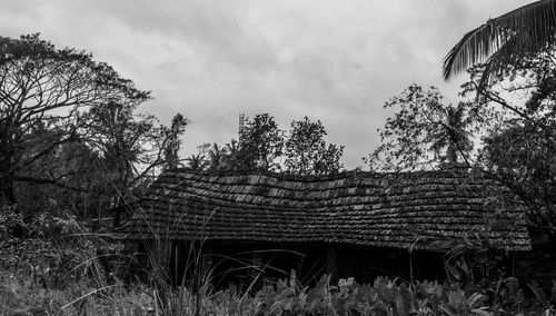 Abandoned house by trees on field against sky