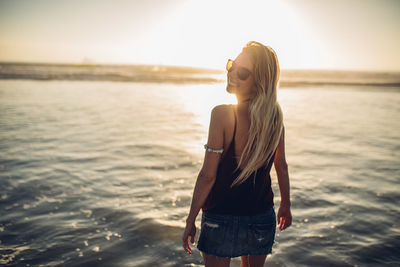 Young woman standing at beach during sunset