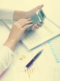 Cropped hands of businesswoman using calculator with documents at desk