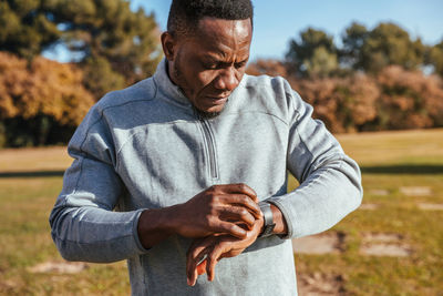 Young man in sportswear checking time while standing on field