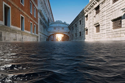 Surface level of canal by buildings against clear sky