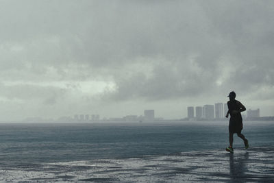 Middle age man runnin under the rain next to the bay view with the blue ocean and cloudy sky