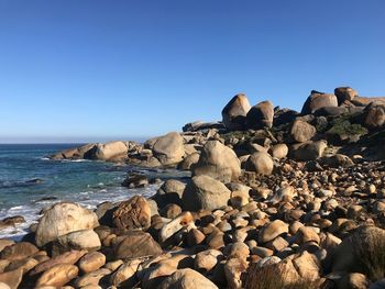 Rocks by sea against clear blue sky