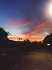 Road by silhouette trees against sky at sunset