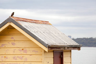 Bird perching on old wooden house against cloudy sky