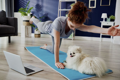 Woman with dog practicing yoga by laptop at home