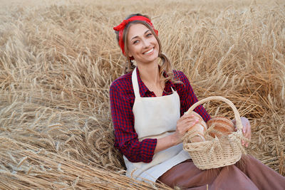 Portrait of smiling woman holding food in basket sitting on plants