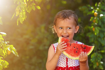 Little curly white girl eating watermelon in the garden , green blurred background