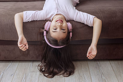 A funny little girl in pink home clothes and pink headphones, lies on the couch