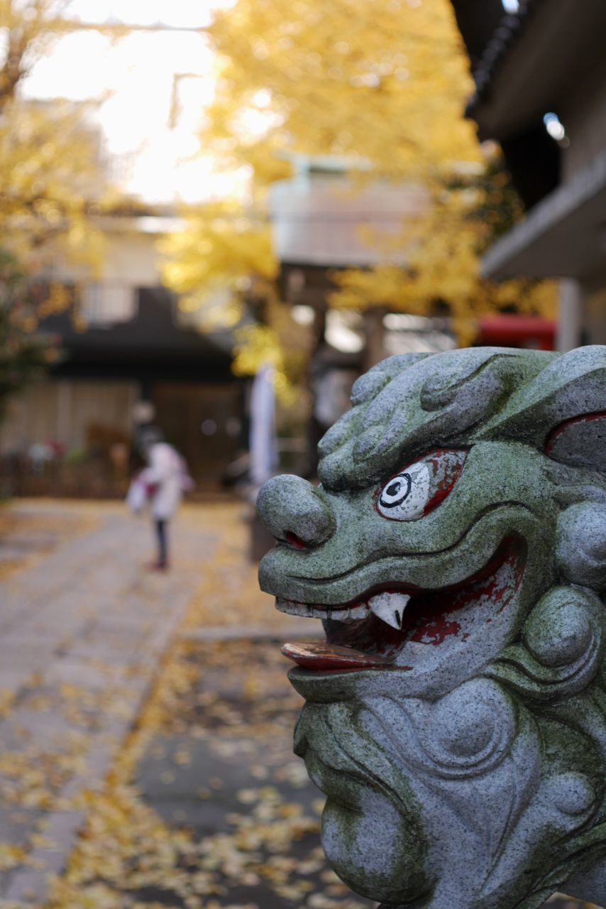 focus on foreground, street, incidental people, close-up, art and craft, selective focus, day, outdoors, creativity, art, road, animal representation, sculpture, human representation, city, tree, sunlight, building exterior, statue