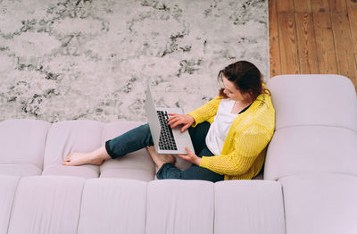 Young woman using mobile phone while sitting on sofa