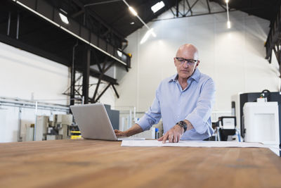 Man with laptop looking at plan on table in factory