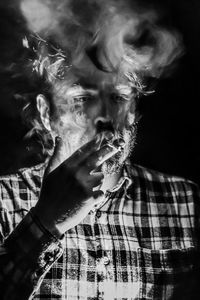 Midsection of man smoking cigarette against black background