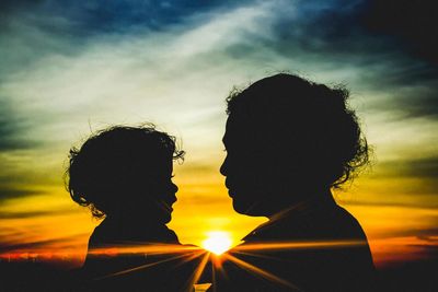 Silhouette woman with daughter standing against orange sky