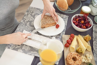 High angle view of woman hand cutting bread in plate on table 