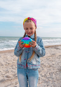 Happy child rainbow pop it toy beach girl walking on sea background antistress sensory simple dimple