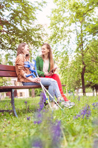 Happy sisters talking while sitting on bench at park