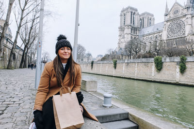 Smiling woman sitting by canal in city during winter