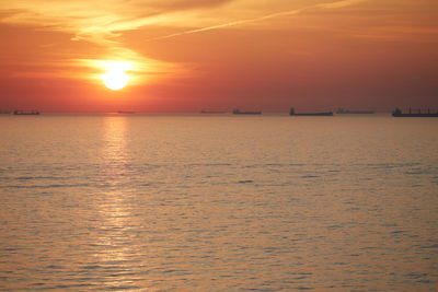 Commercial ships anchored at sea at sunset.