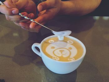 Cropped image of person making teddy bear art on cappuccino