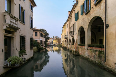 Buildings by canal against sky in city