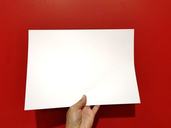 Low section of person holding paper against red background