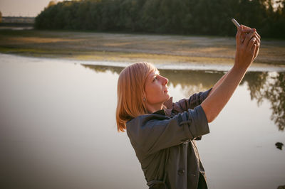 Woman photographing with mobile phone by lake