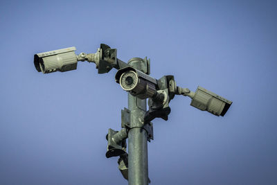 Low angle view of security cameras on pole against clear blue sky