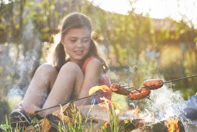 Girl preparing food in bonfire against plants