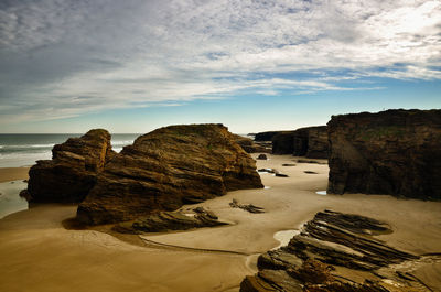 Rocks on shore by sea against sky