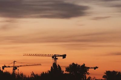 Silhouette crane at construction site against sky during sunset