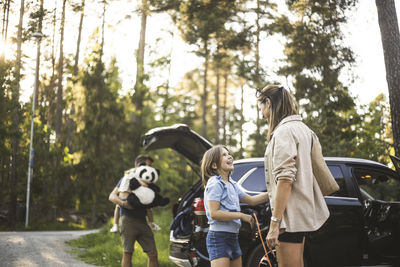 Portrait of mother, father and two daughters standing by car at electric vehicle charging station