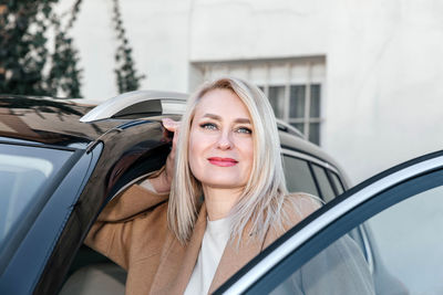 Confident mature woman with striking eyes leaning on a sleek car door