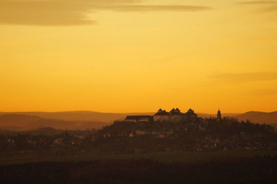 Silhouette built structure on landscape against orange sky