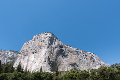 Low angle view of rocky mountain against clear blue sky